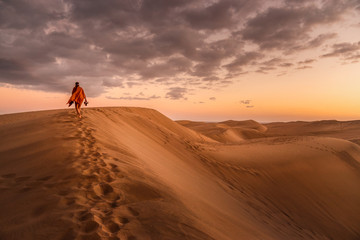 young woman from behind walking in sand dunes of maspalomas, gran canaria - obrazy, fototapety, plakaty