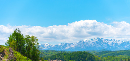 Fototapeta premium Panoramic rural landscape with mountains. Vast blue sky and white clouds over farmland field in a beautiful sunny day in springtime.