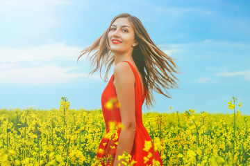 Naklejka na ściany i meble Young beautiful girl in a red dress close up in the middle of yellow field with radish flowers and highlights