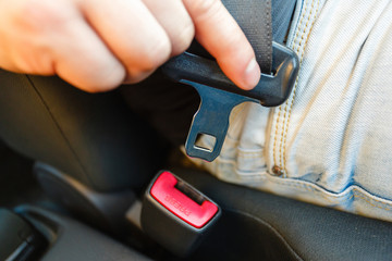 Close-up of car seat belt fastener. Men's hand fastens the seat belt of the car. Close your car seat belt while sitting inside the car before driving and take a safe journey.