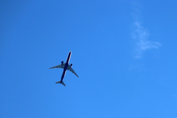 Fototapeta na wymiar Airplane in the clear blue sky. Commercial jet plane in a flight close up, bottom view