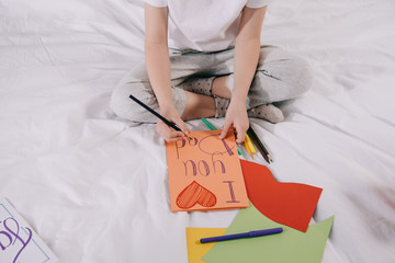 partial view of kid drawing fathers day greeting card while sitting on bed