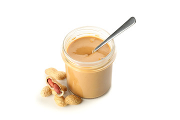 Creamy peanut butter in glass jar, peanut and spoon isolated on white background. A traditional product of American cuisine