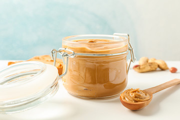 Composition with peanut butter sandwich, glass jar, peanut and spoon on white table against light background, space for text and closeup