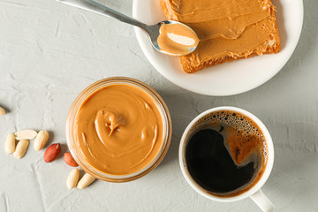 Glass jar with peanut butter, peanut, cup of coffee, spoon and peanut butter sandwich on grey...