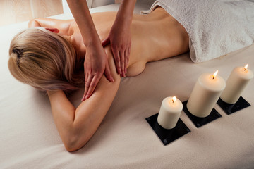 Obraz na płótnie Canvas beautiful blonde female relaxation in spa salon with professional masseur shoulder body next to the candle fire