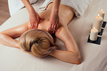 Obraz na płótnie Canvas Ayurvedic relaxing.health beauty happy blonde woman in spa salon getting massage .Beautiful girl enjoying day spa resort, lying down on the table treatment procedure next to the candle fire