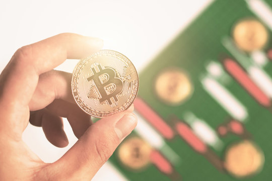 Close up hand holding bitcoin with background Candlestick chart make from color paper white and red on Green board with grid lines