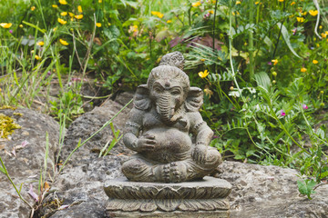 Ganesh stone statue in a garden with green grass and flowers