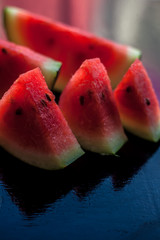 Mouth-watering watermelon tea in a transparent glass cup on wooden surface with watermelon pieces in triangle shape.