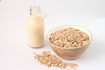 Oat flakes in glass jar and bottle of milk on white background