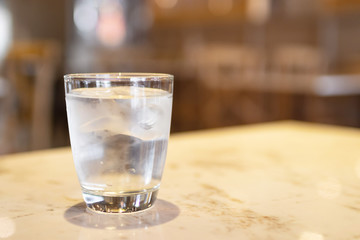 Glass of water with ice cubes on marbled table at restaurant with copy space. 