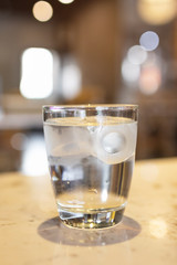 Glass of water with ice cubes on marbled table at restaurant. 