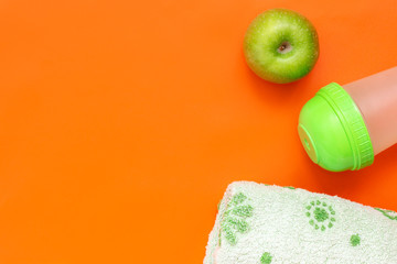 Healthy lifestyle concept. Green apple, towel and shaker on orange background