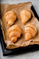 freshly baked golden croissants on black metal pallet on parchment