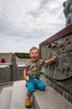 Happy smiling caucasian toddler boy looking at camera next to a Chinese statue monument.