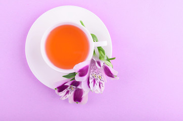 Beautiful flowers of astromeria. Herbal tea in a white cup and a white saucer on a pink background