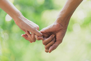 Closeup two person hook each other's little finger on nature background.