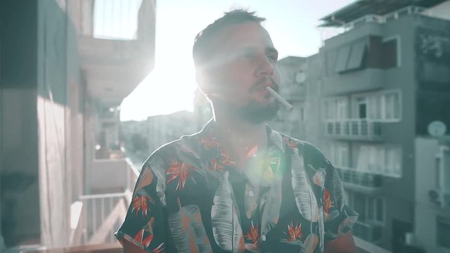 Close up handsome young man smoking cigarette at sunset. He wearing floral shirt in summer