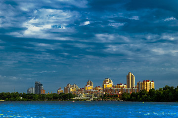 Fototapeta premium Cityscape on sunny day against blue cloudy sky with lake in foreground