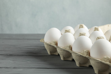 White chicken eggs in carton box on wooden table against light background, space for text