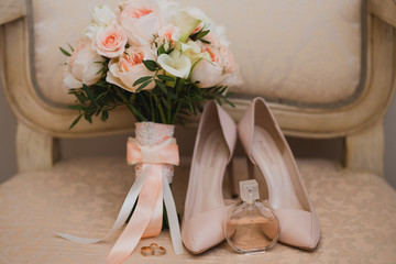 Botanic bridal chic. Bouquet with silk ribbons, female classic shoes, perfume bottle, wedding rings on vintage chair.