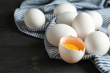 White chicken eggs in carton box and kitchen towel on wooden table, space for text and closeup