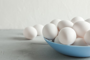 White chicken eggs in plate on grey table against white background, space for text