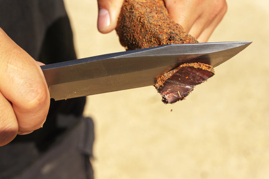 A man cuts a basturma with a large knife. Close-up