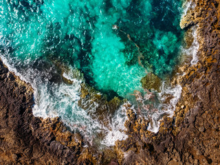Azure clear water hits the rocky coast of coral beach. Aerial top view