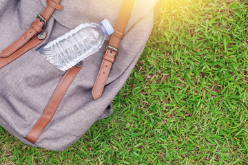 A gray backpack and a bottle of water on green grass background top view,