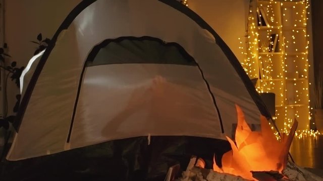 Lockdown of tent located in living room near artificial campfire and shadows of kids playing inside of it
