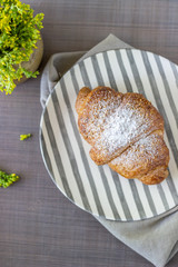 A croissant and coffee on a grey background. The flowers. Breakfast.
