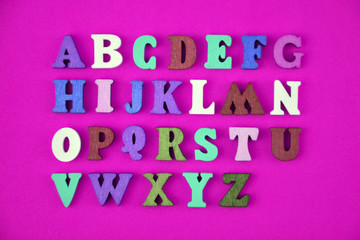 English alphabet made of multi-colored wooden letters on purple background