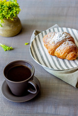 A croissant and coffee on a grey background. The flowers. Breakfast.