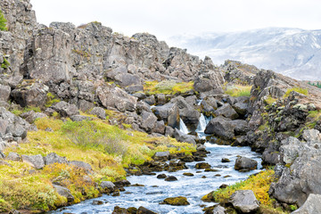 Thingvellir National Park with autumn foliage in Iceland Golden circle and small waterfall on rocky trail with blue water landscape
