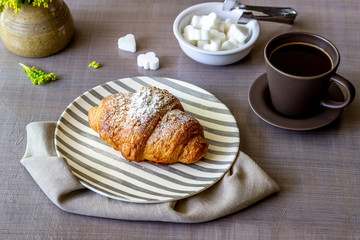 A croissant and coffee on a grey background. The flowers. Breakfast.