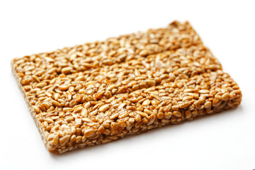 A large golden tile of sunflower seeds, a bar in a sweet molasses on a white background. Kozinaki useful and tasty sweets of the East