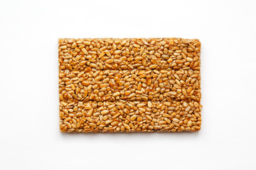 A large golden tile of sunflower seeds, a bar in a sweet molasses on a white background. Kozinaki useful and tasty sweets of the East
