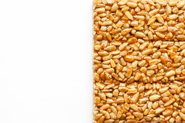 A large golden tile of sunflower seeds, a bar in a sweet molasses on a white background. Kozinaki useful and tasty sweets of the East