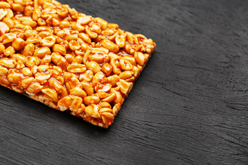 A large golden tile of peanuts, a bar in a sweet molasses on a black texture background. Kozinaki useful and tasty sweets of the East