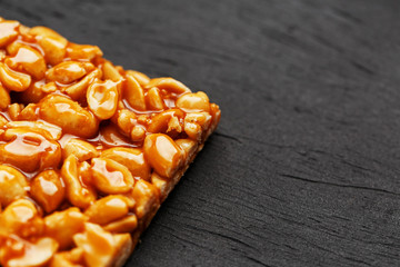 A large golden tile of peanuts, a bar in a sweet molasses on a black texture background. Kozinaki...