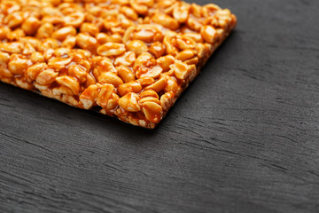 A large golden tile of peanuts, a bar in a sweet molasses on a black texture background. Kozinaki useful and tasty sweets of the East