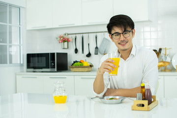 An asian man is drinking orange juice in the kitchen