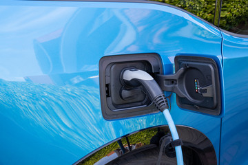 Fototapeta na wymiar Blue EV car or electric car at charging station with the power cable supply plugged in. Electro mobility environment friendly.- Image