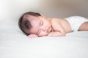 cute newborn baby is sleeping on white bed