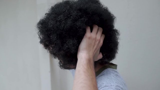 Young man scratching his head and fluffy curly black hair