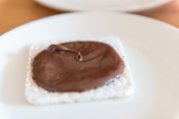 Closeup of rice cake with chocolate hazelnut spread with brown syrup vegan vegetarian snack dessert one single piece on white plate