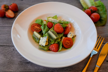 fruit and vegetable salad with strawberries, kiwi, cherry tomatoes and feta cheese in a white plate on a wooden table