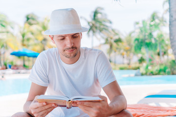 Caucasian guy relaxing near pool with amazing view and reading book